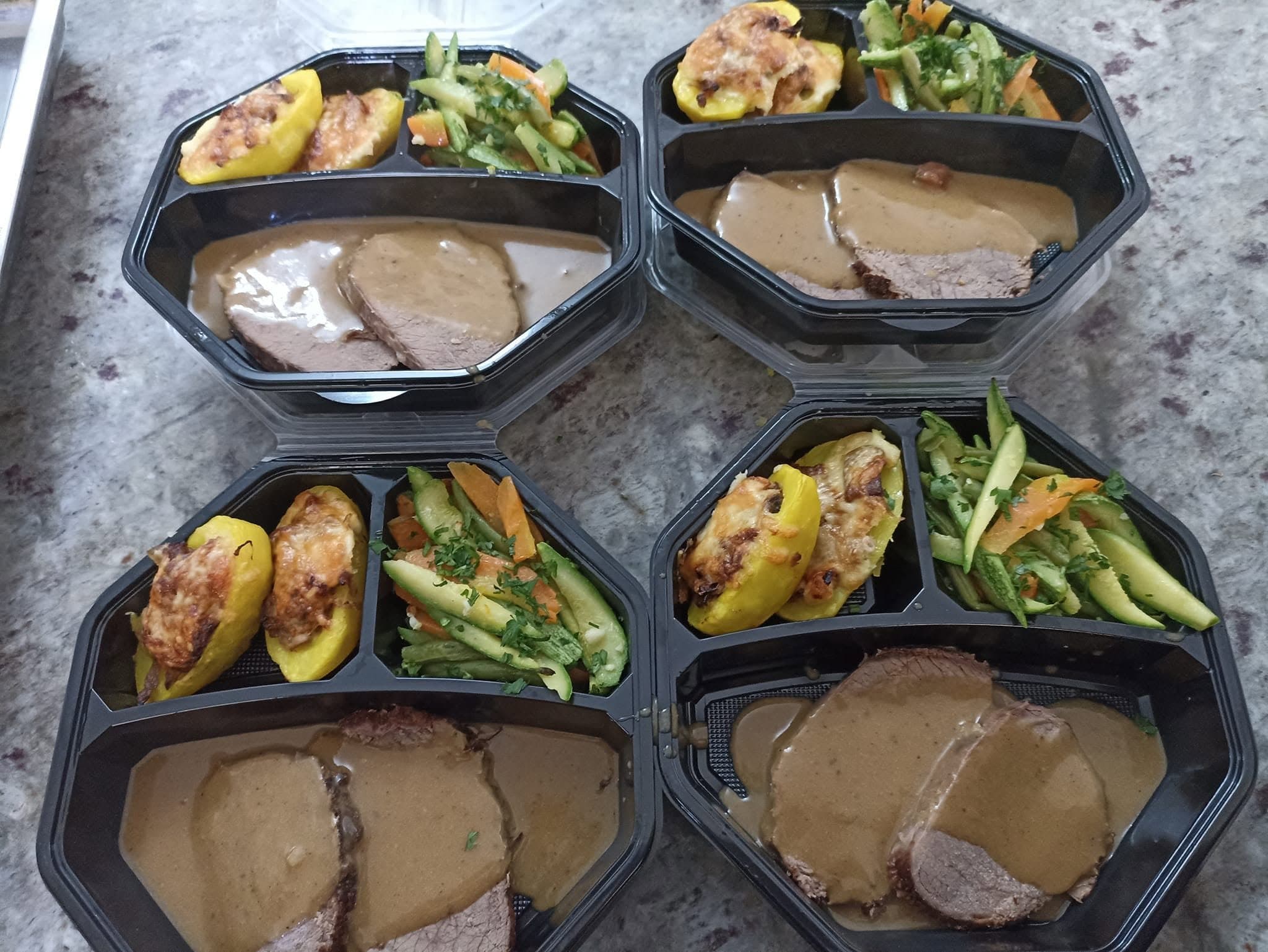 Quatre coffrets repas : viande en sauce, pommes de terre farcies et légumes sautés.