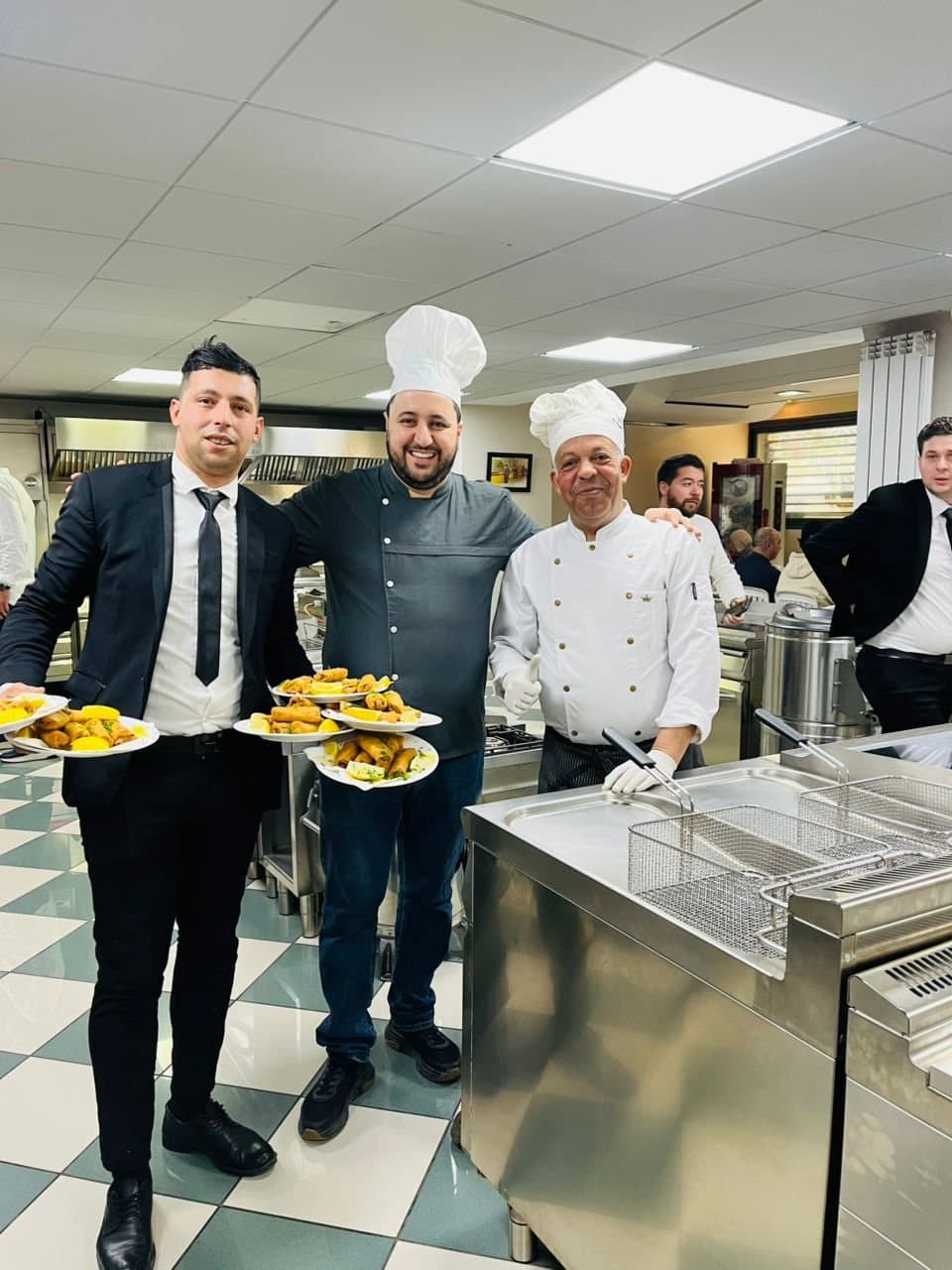L'équipe en cuisine : deux chefs et un responsable de salle tiennent des assiettes prêtes à servir.