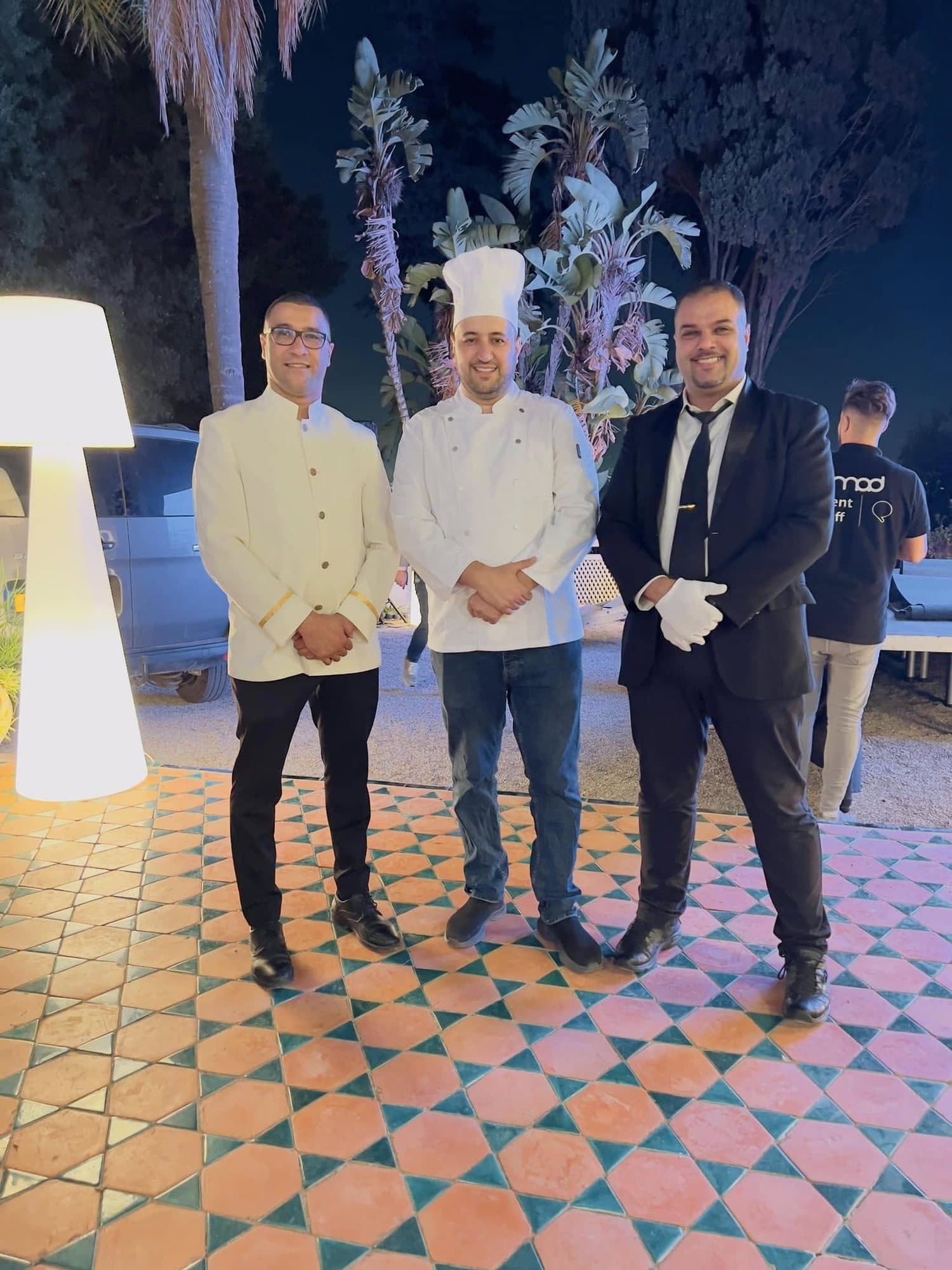 Trois membres de l'équipe, dont un chef, lors d'une réception en soirée dans un jardin.