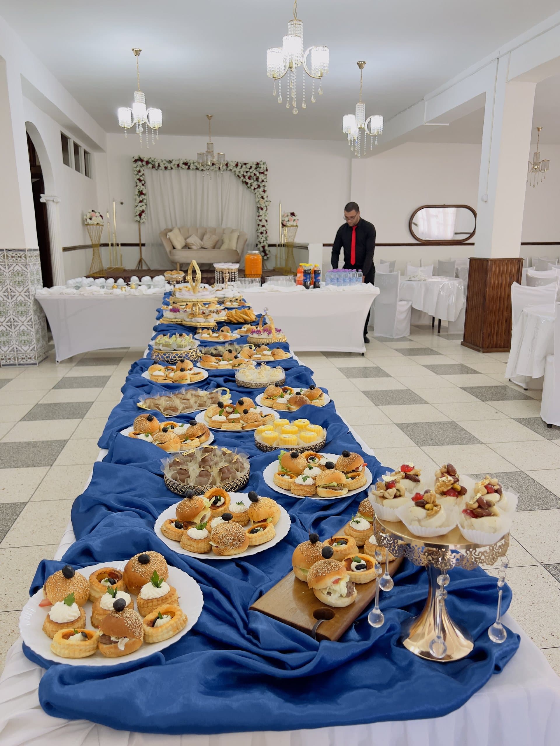 Une longue table de fiançailles drapée de bleu, garnie de pâtisseries et de verrines.