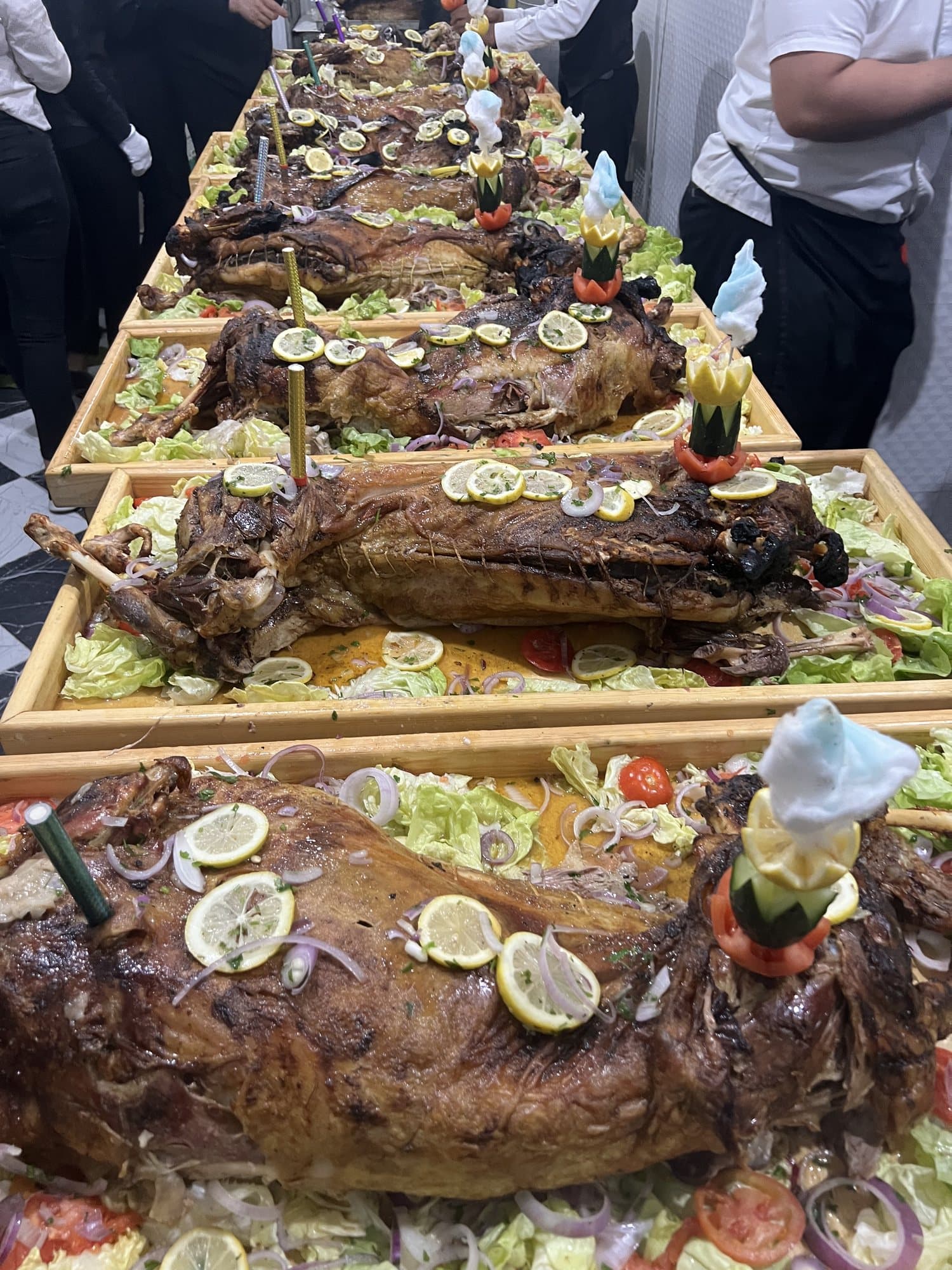 Une longue table de méchouis garnis de citrons et de légumes, au milieu de l'équipe de service.