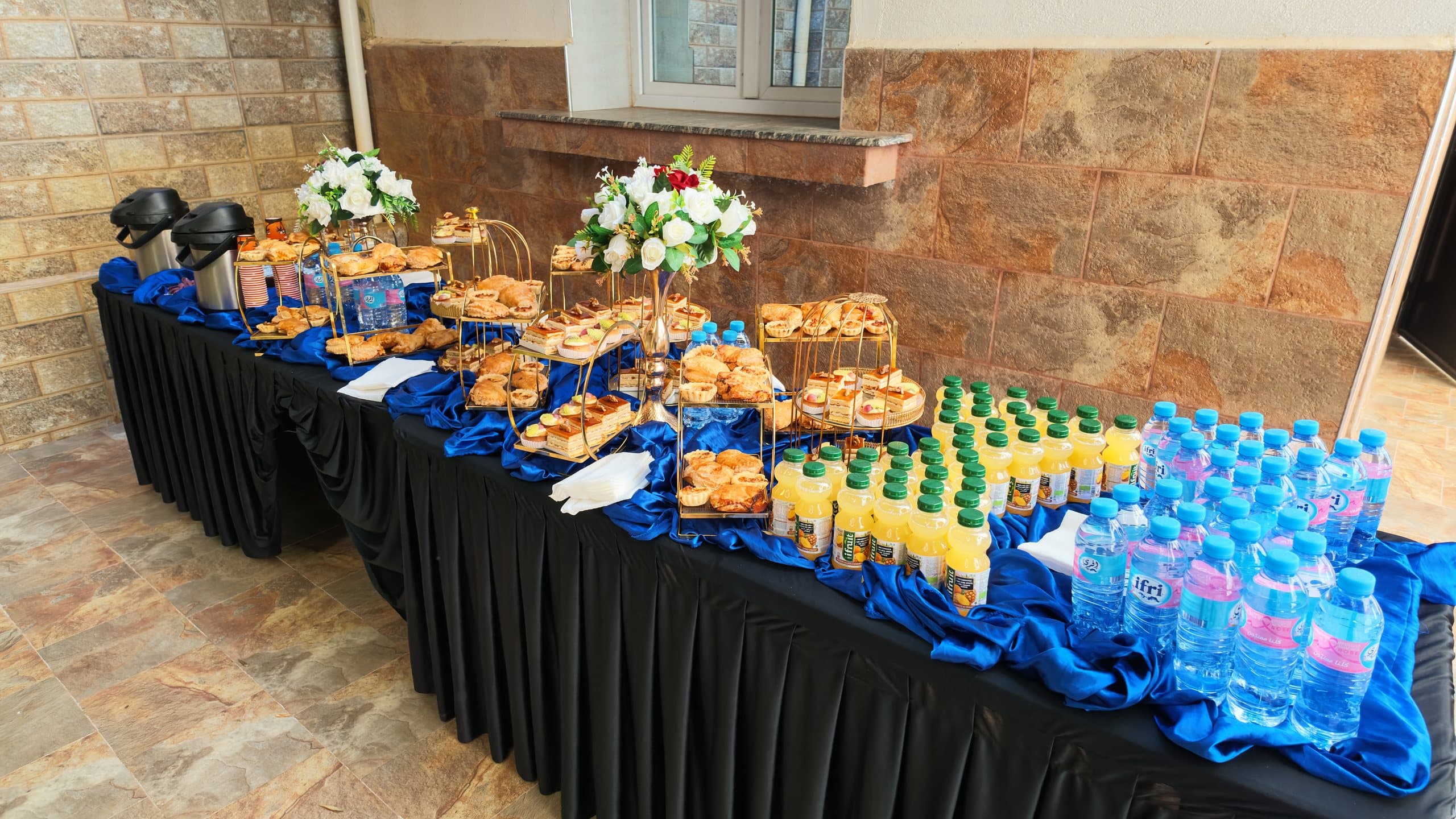 Une table de pause-café dressée : viennoiseries, jus, bouteilles d'eau et thermos de café.