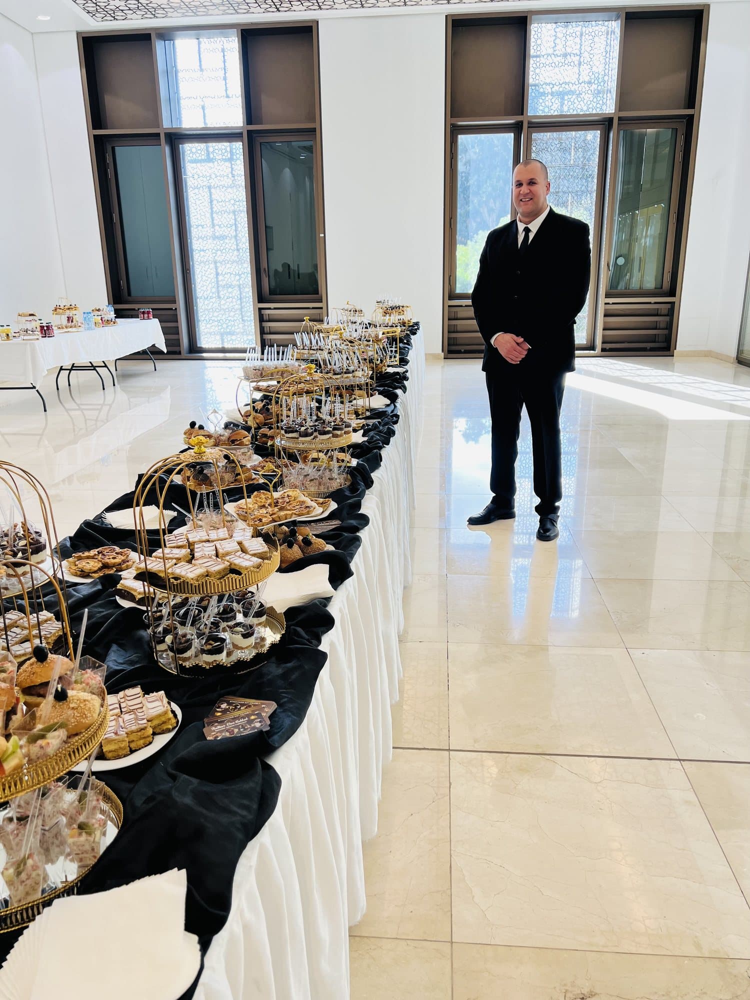 Un responsable de salle à côté d'un long buffet nappé de noir dans un hall lumineux.