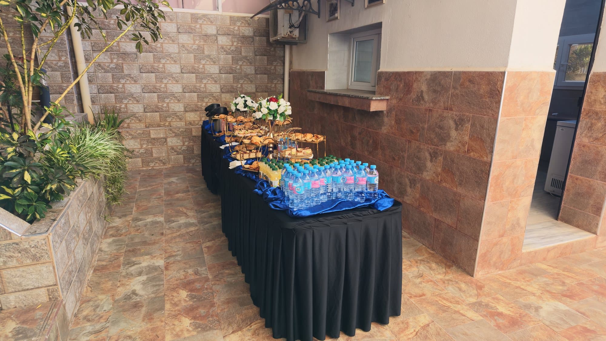 La même table après installation : viennoiseries sur présentoirs dorés, bouquets, jus et bouteilles d'eau.