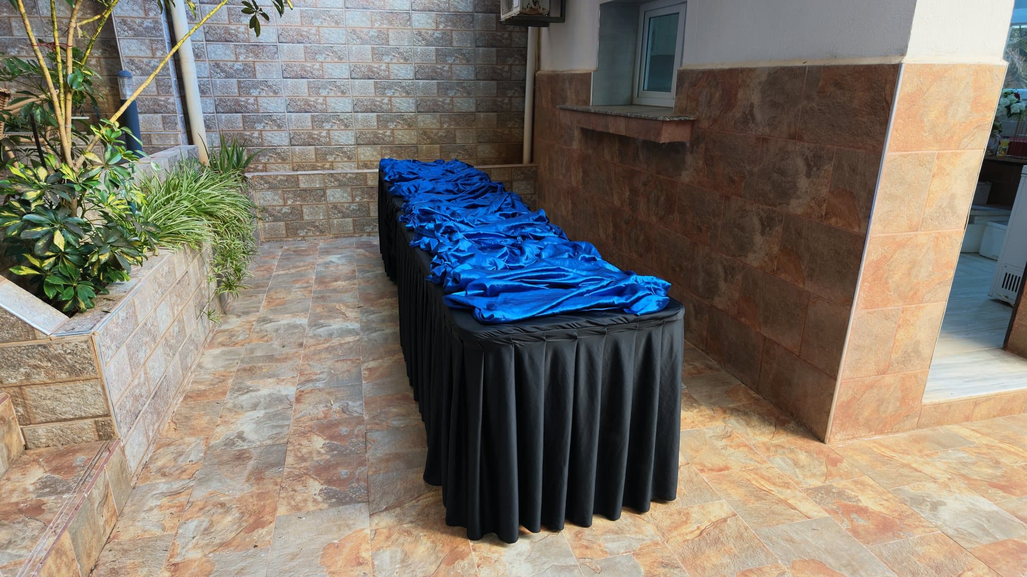 La table avant installation : nappe noire plissée et tissu bleu, encore vide, dans une cour.