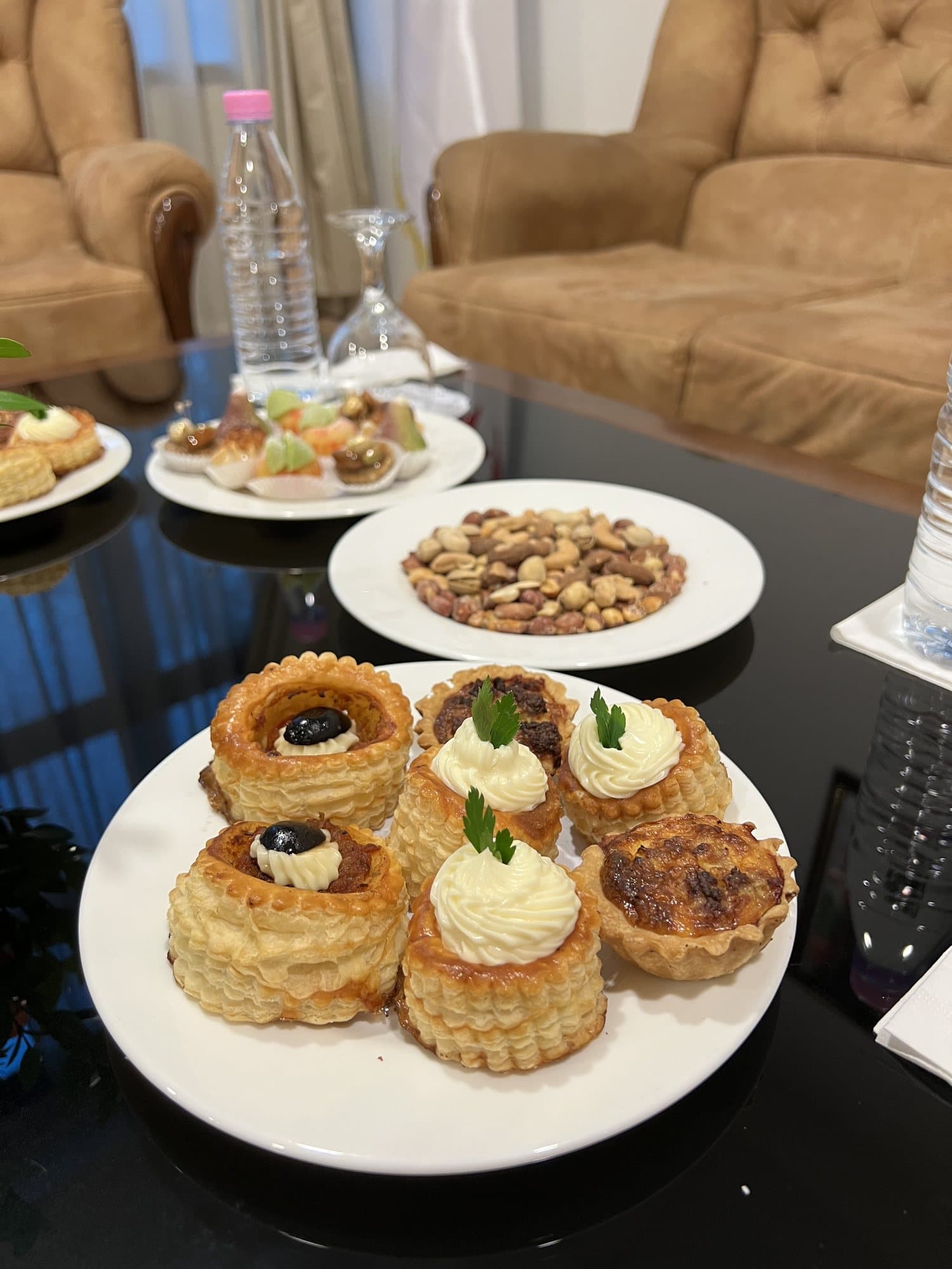 Une assiette de bouchées salées et une coupelle de fruits secs servies dans un salon.
