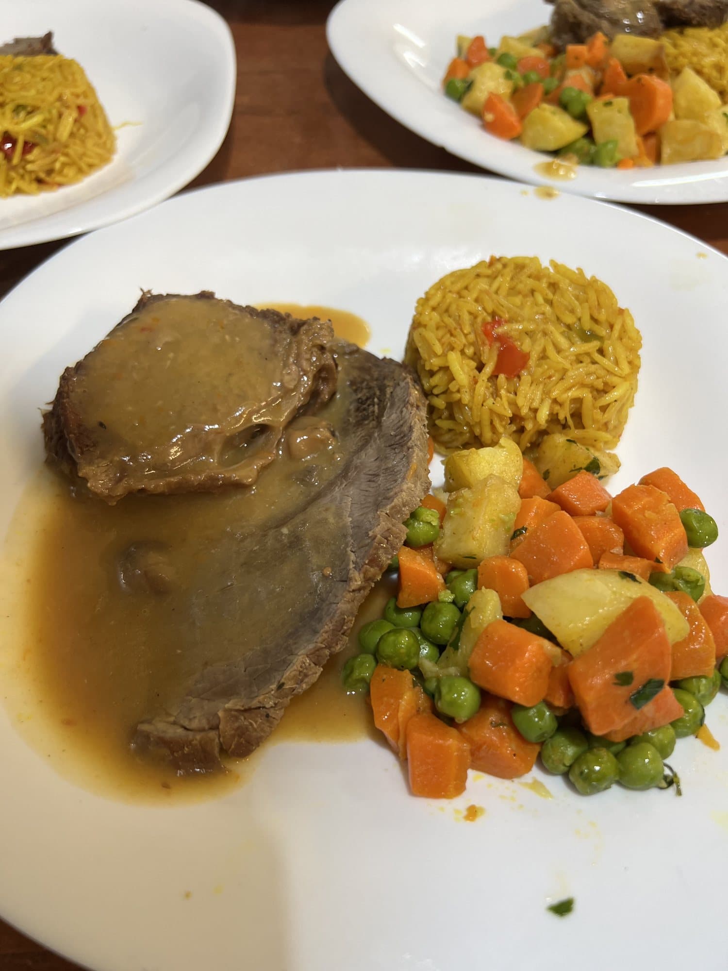 Une assiette de viande en sauce, riz safrané, petits pois et carottes.