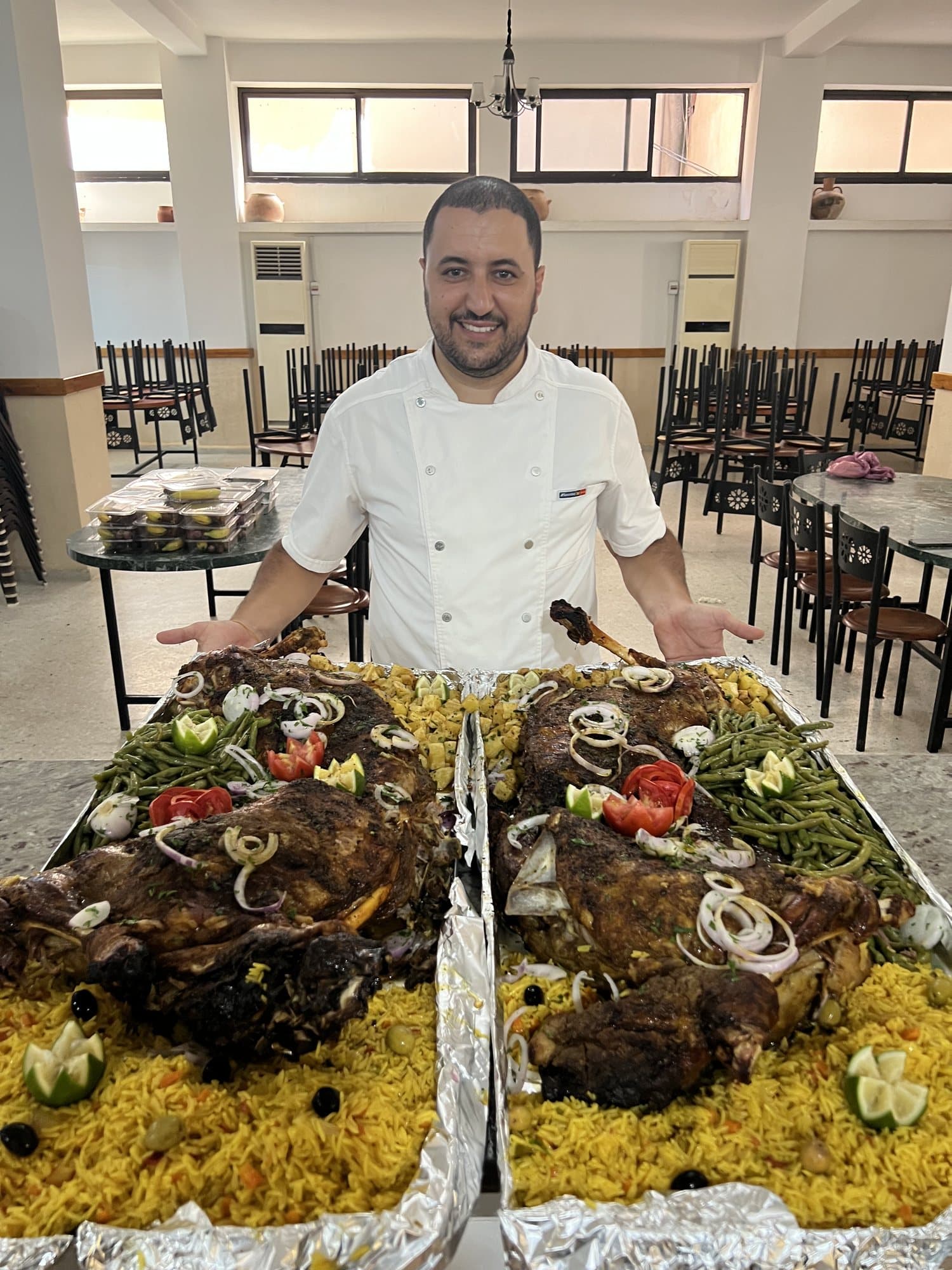 Un chef présente deux grands plateaux de viande rôtie sur riz, garnis de légumes.