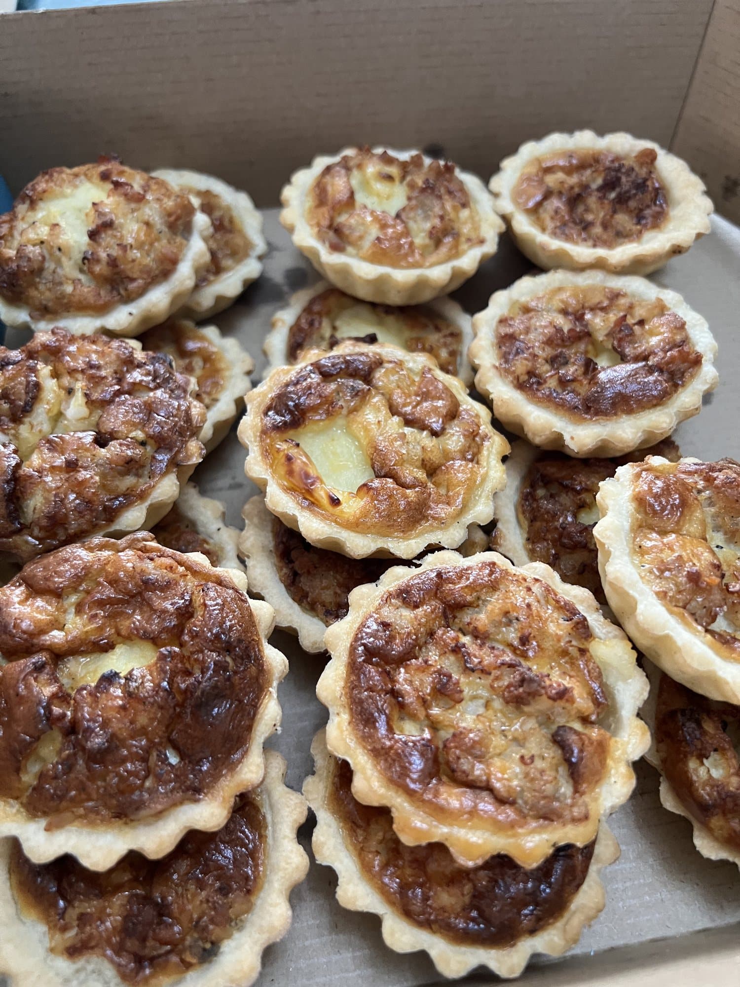 Des mini-quiches dorées, alignées dans leur boîte.